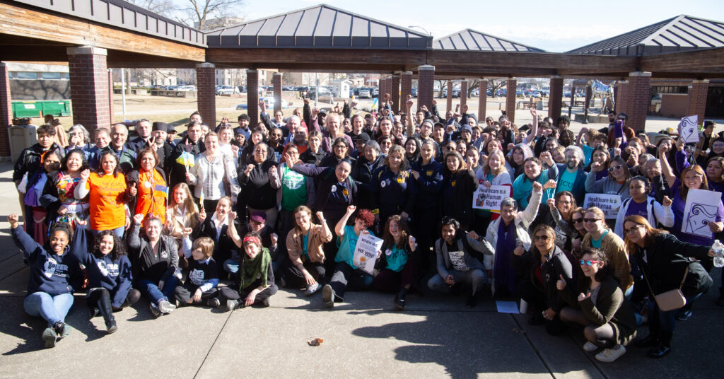 A crowd of around 100 people take a group photo together in a courtyard.