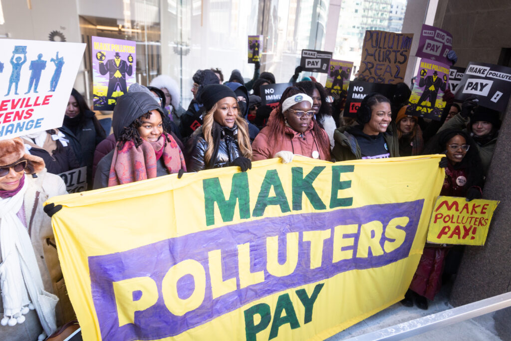 A crowd of folks holding signs and banners that say Make Polluters Pay.
