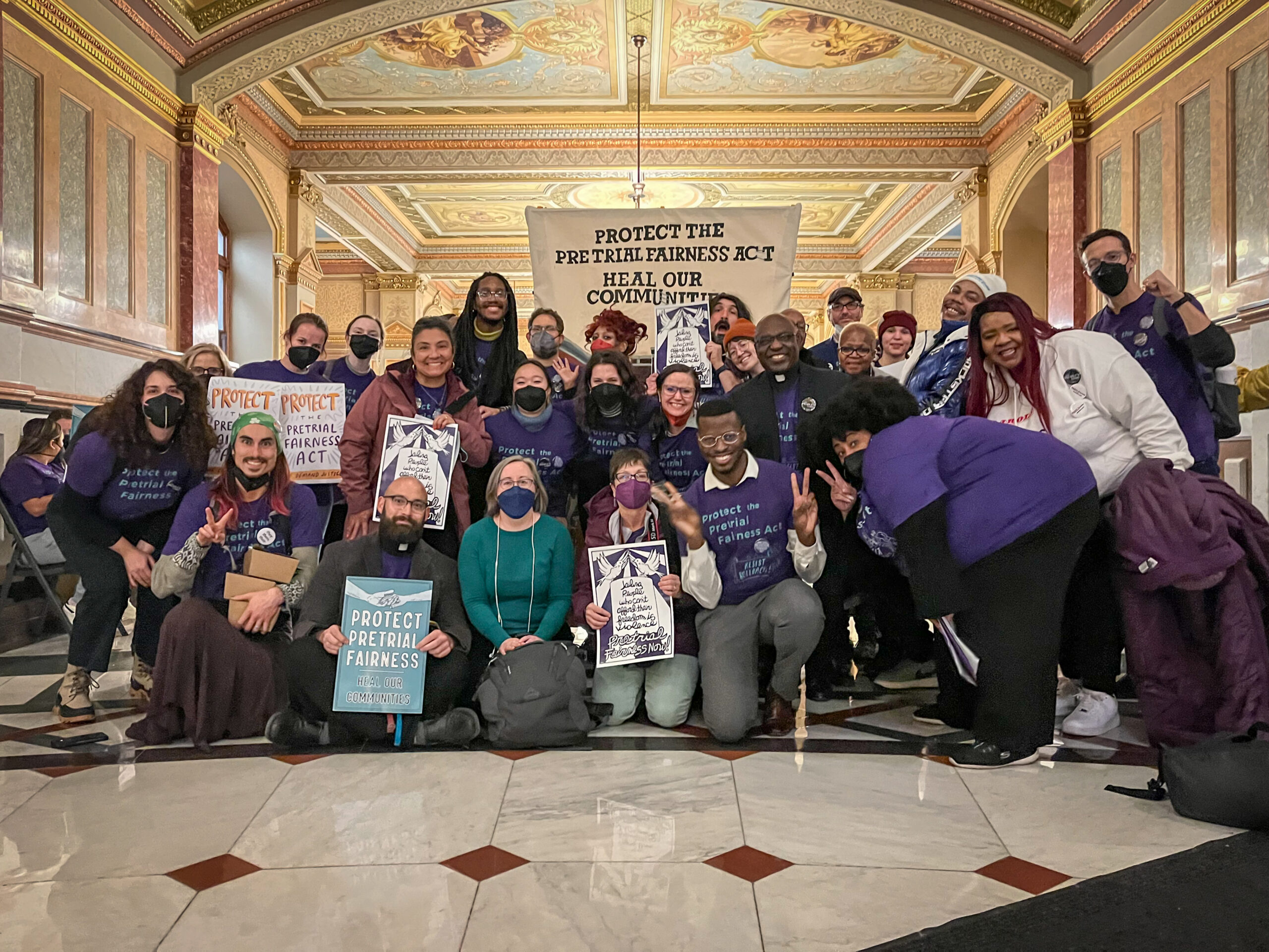 Several advocates with signs and t-shirts that read “Protect Pretrial Fairness, Heal our Communities” smiling at the camera.