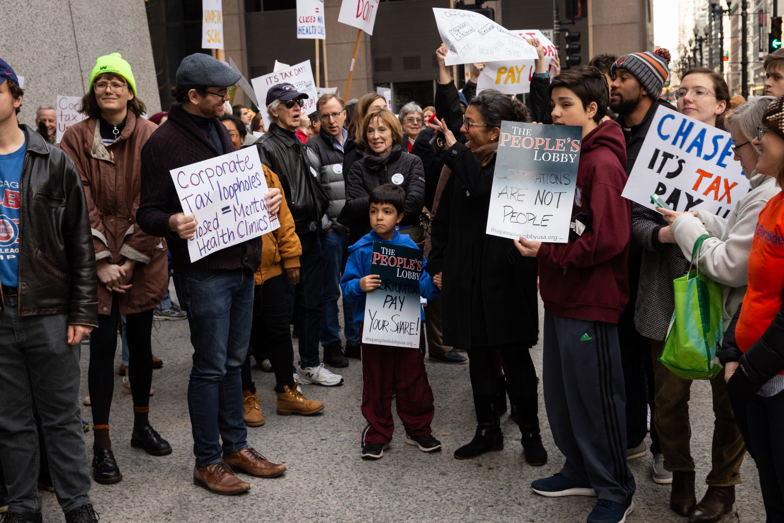 A group of people holding signs about corporate tax and protesting in front of a building