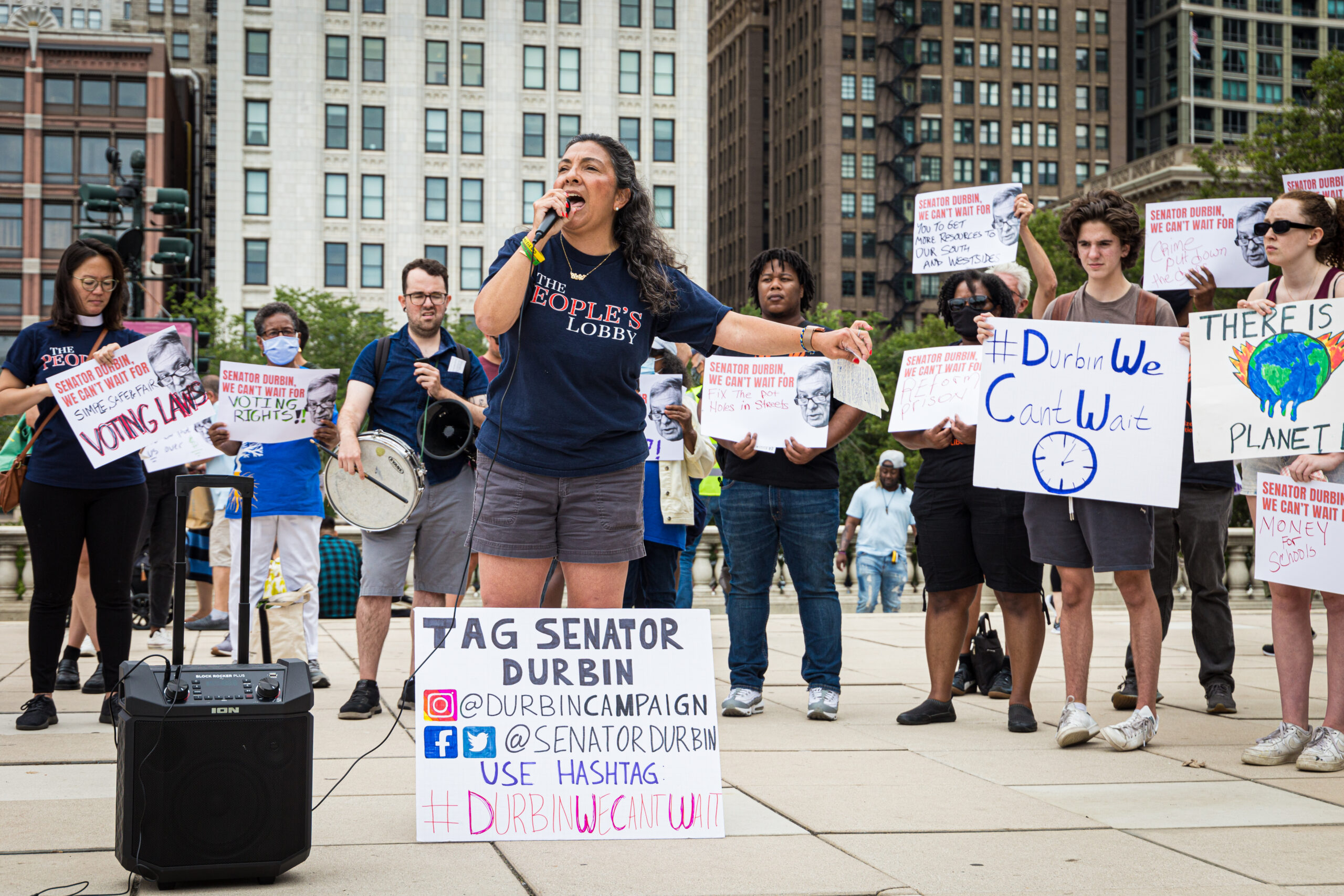 A person holding a mic connected to an amplifier in the center of a group of activists holding signs about climate change.