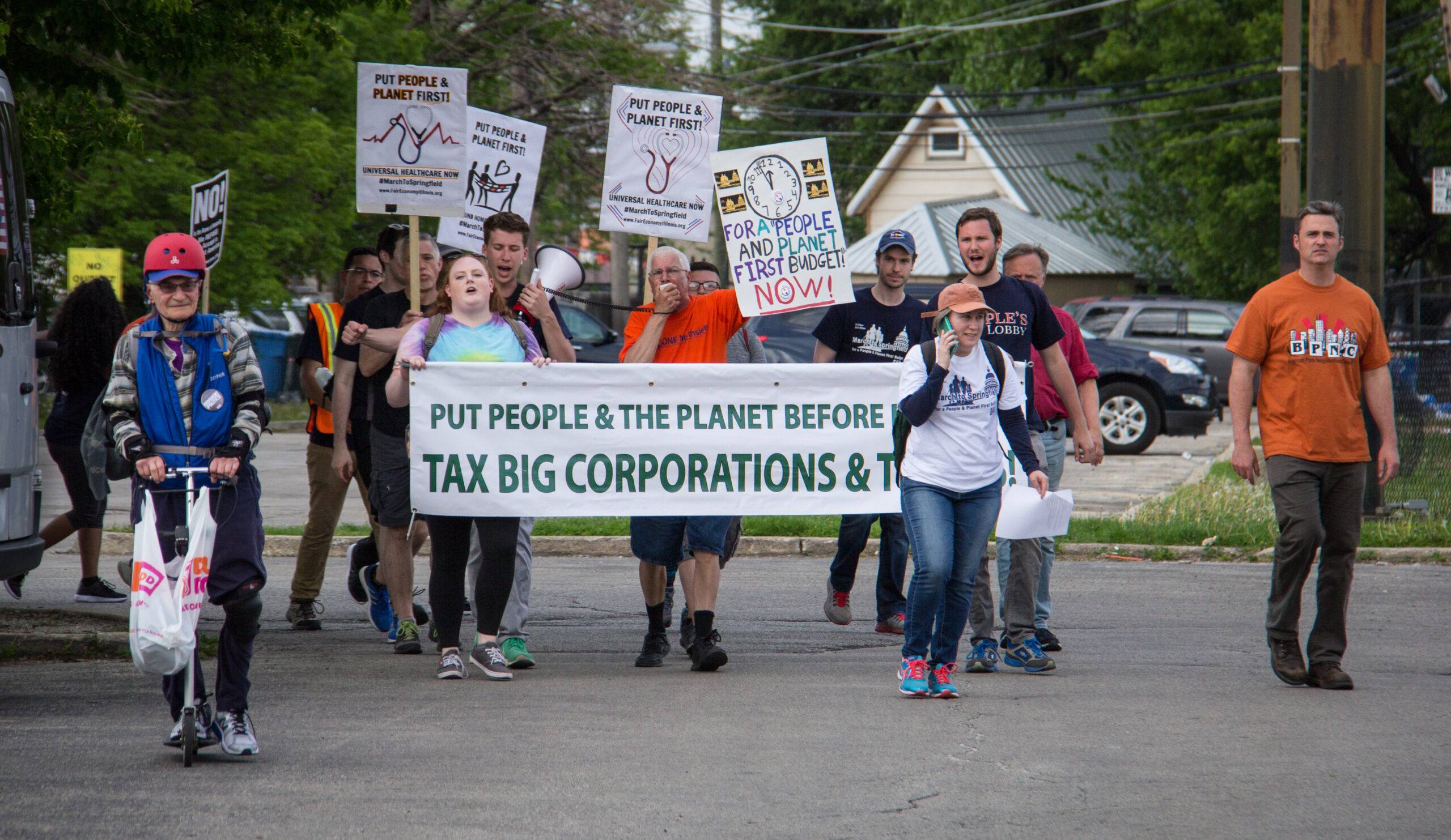 A group of people with megaphones and signs related to March To Springfield and Universal Healthcare.