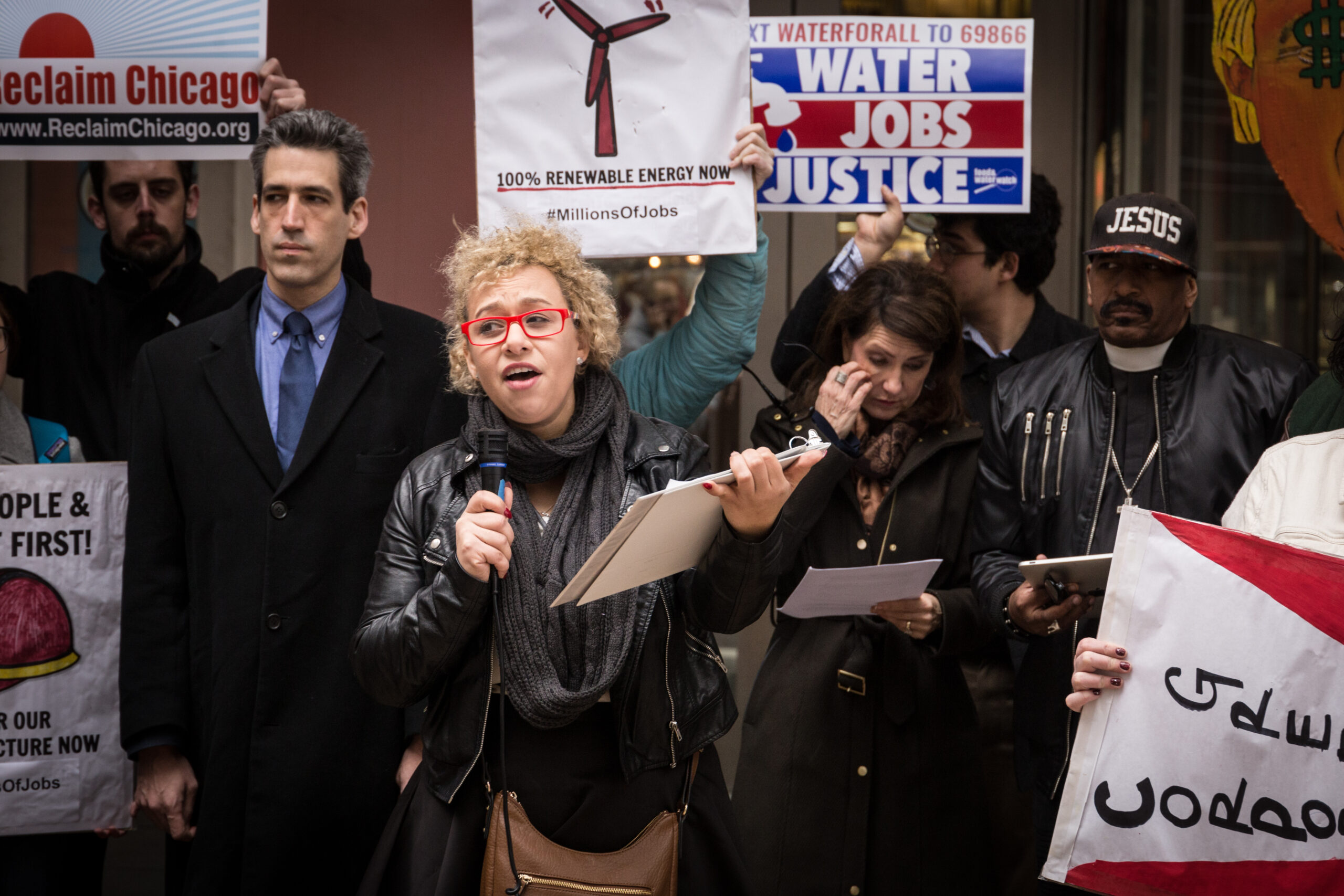 Group of protestors with a person holding a clipboard and mic in the center.