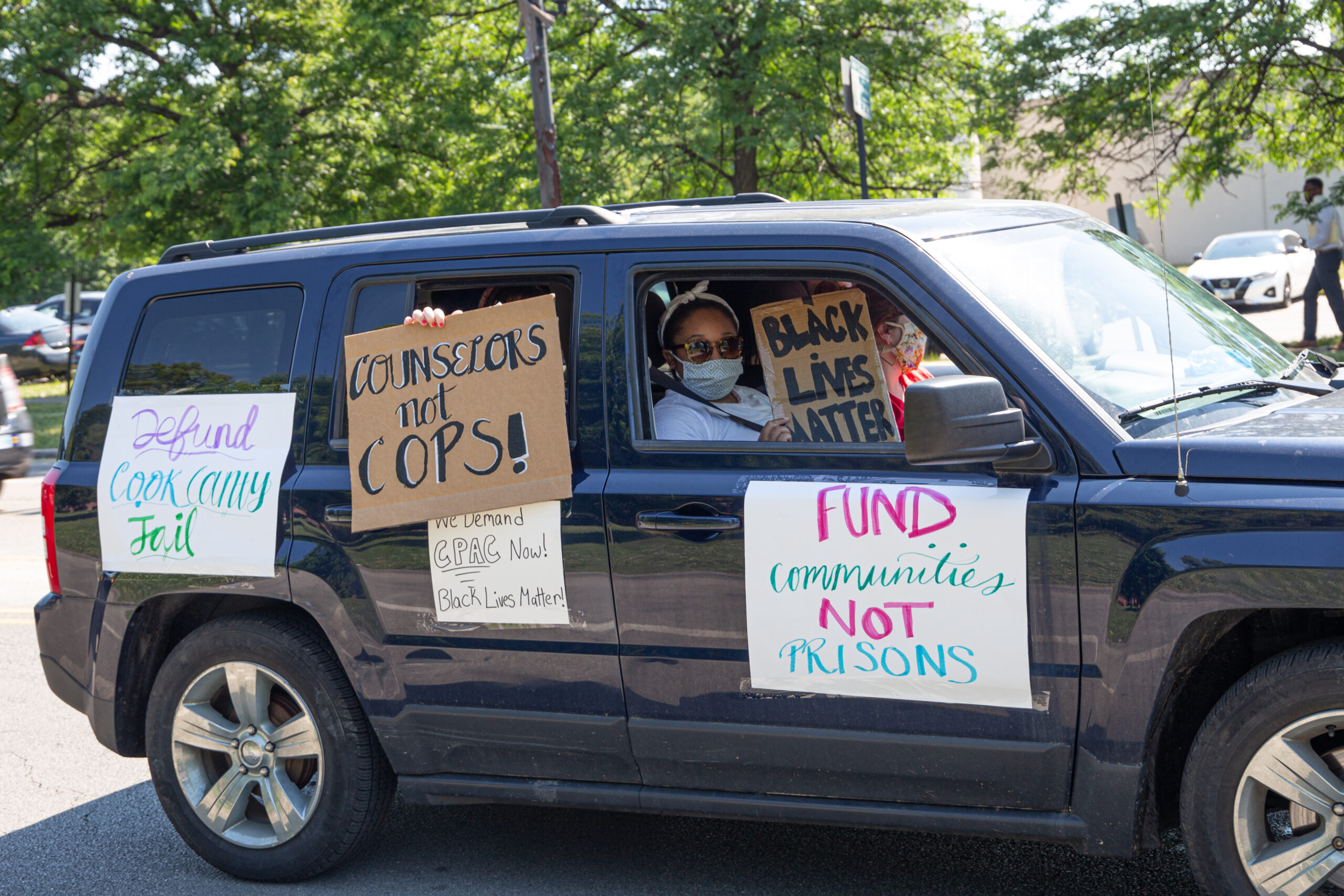 A black van with the passengers holding “Black Lives Matter” and “Counselors not Cops” signs, along with other signs taped to the doors.