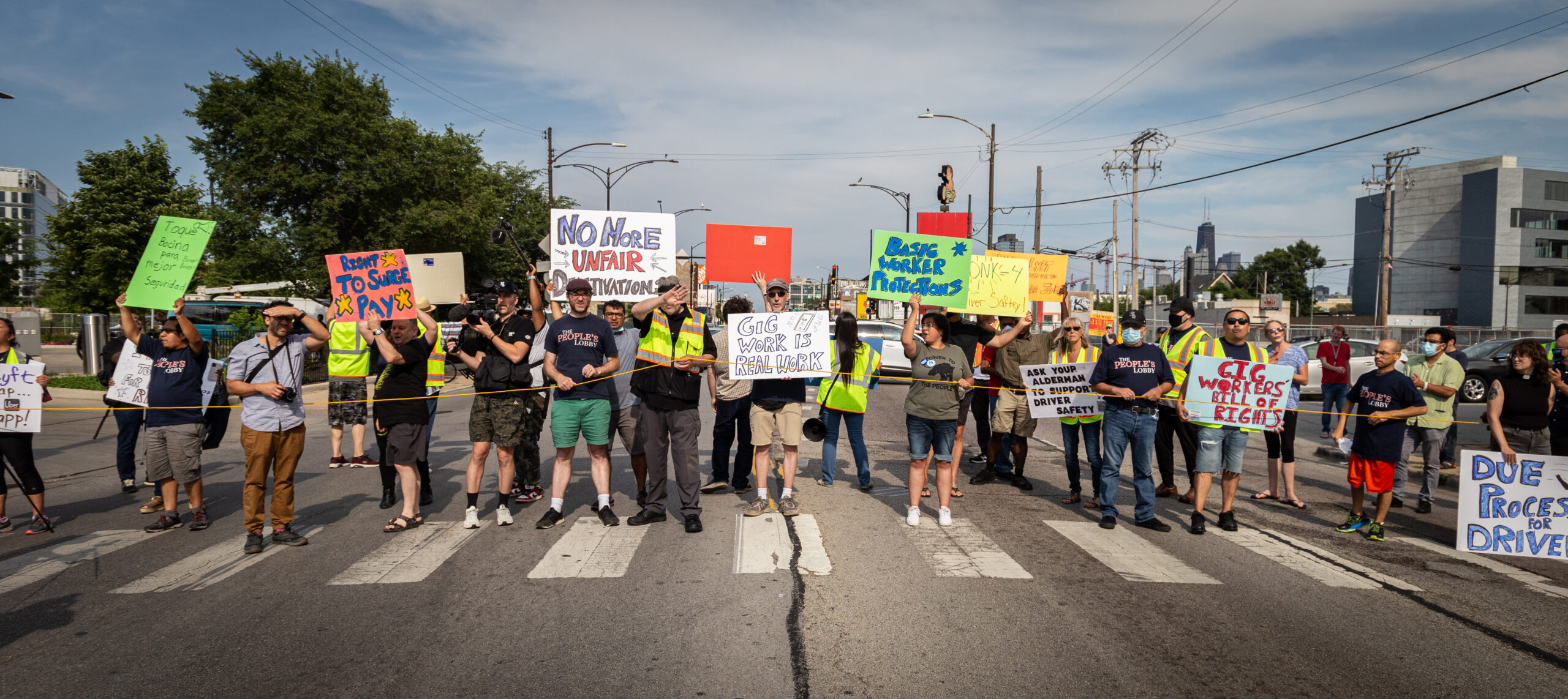 Several people holding signs about Gig Workers Rights standing in a line on a road crossing.