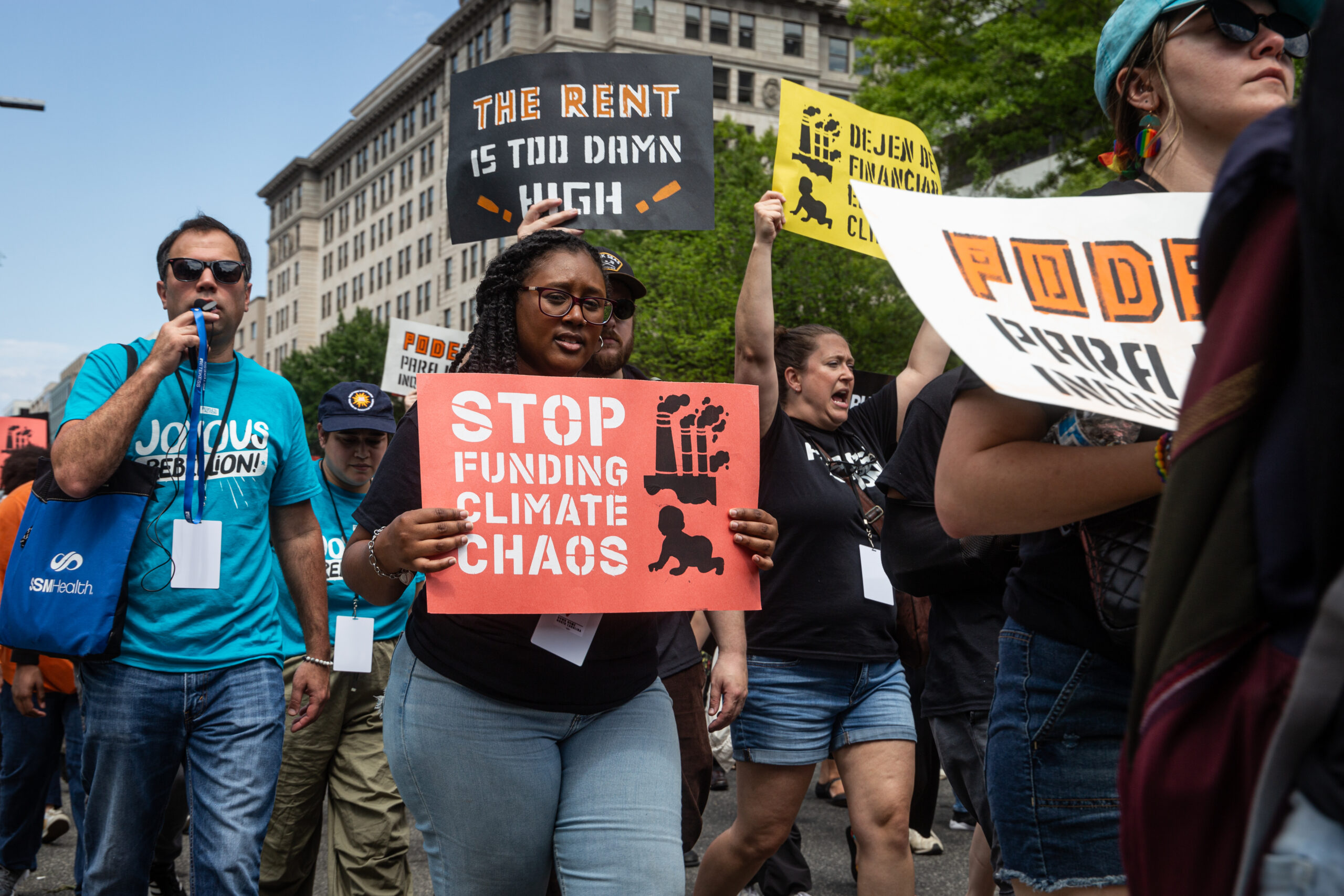 A person holding a sign that says “Stop funding climate chaos” surrounded by other climate activists with signs walking in the same direction.