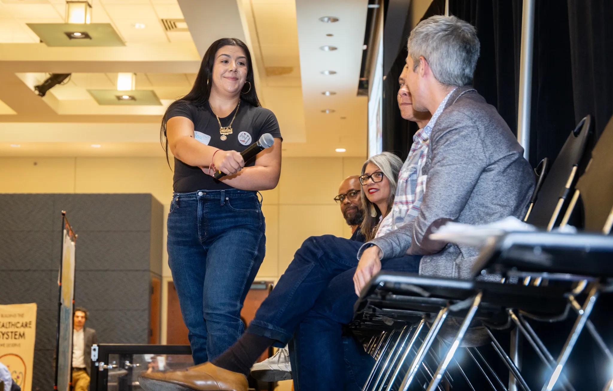 Person holding mic towards a person in a panel of people sitting on chairs.