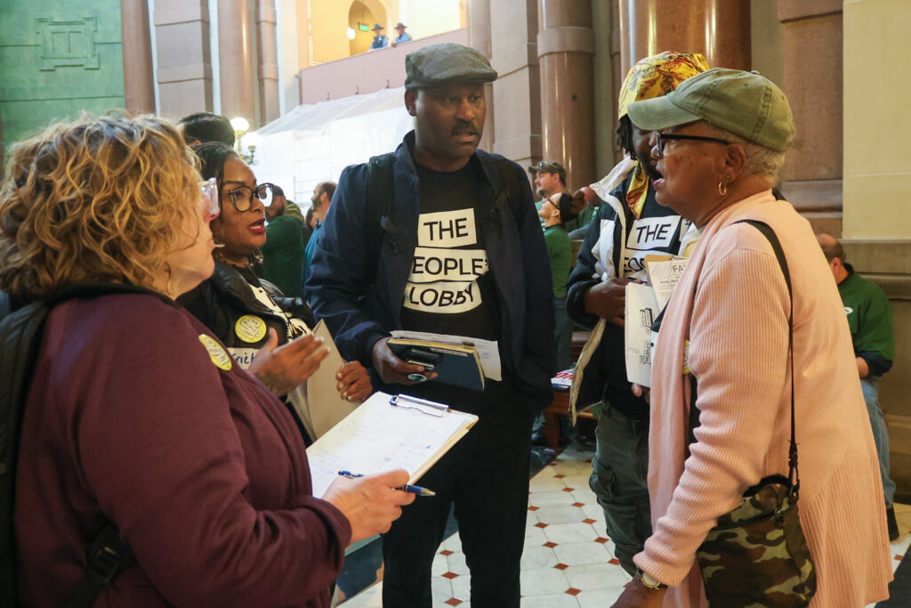 Five organizers wearing The People's Lobby T-Shirts father in a circle and talk with each other inside the Capitol Building.