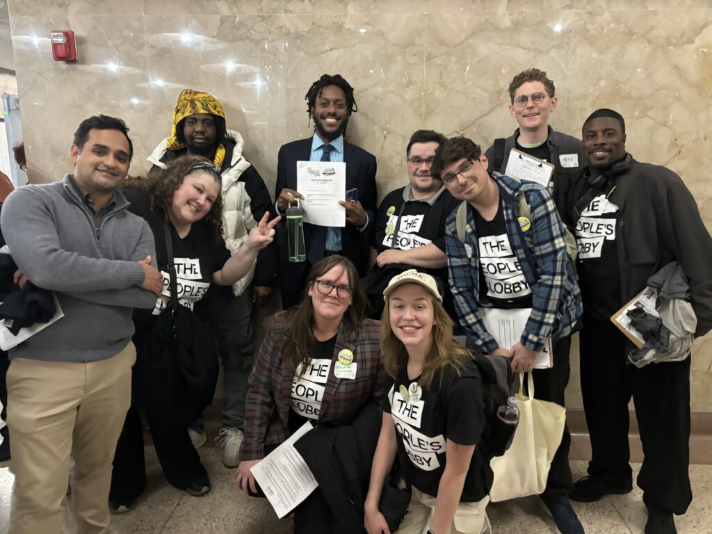 Nine organizers smile in a group, surrounding State Senator Mike Simmons, who is holding up a piece of paper.