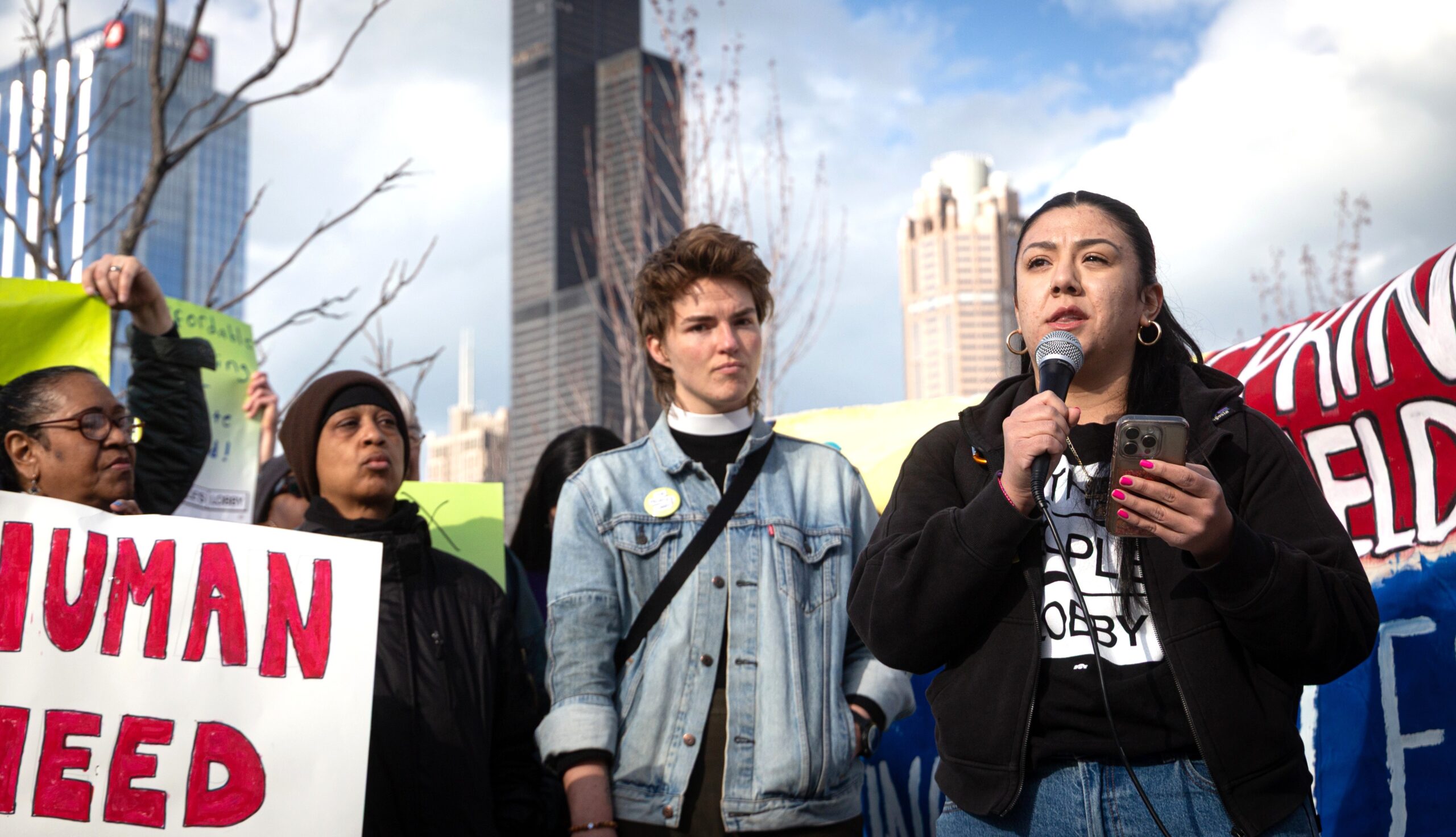 Lina Avalos speaks in front of a crowd of people holding protest signs.