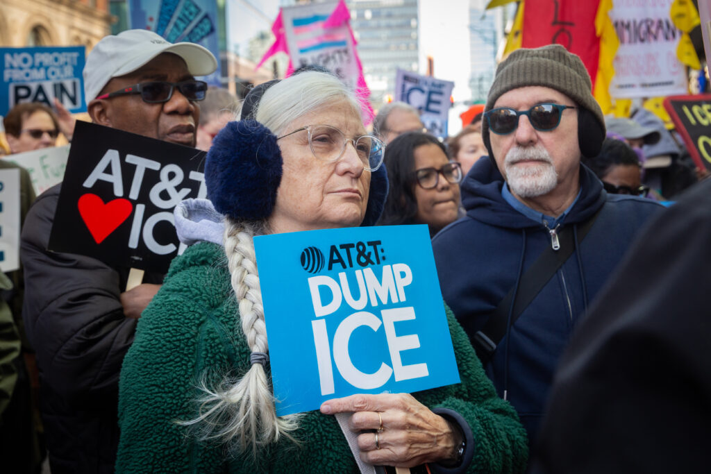 A person holding a sign that says "AT&T: DUMP ICE".